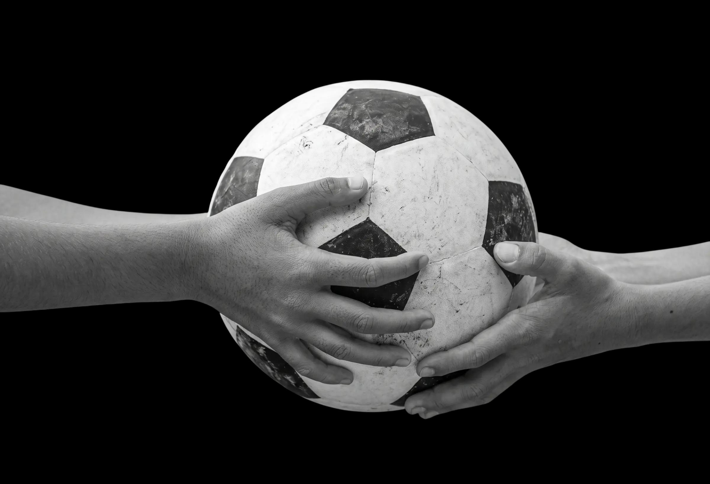 Hands from two sides holding a soccer ball